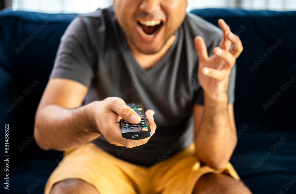 Fototapeta premium Young man watching television with various action. Man holding TV remote changing program menu enjoy watching.