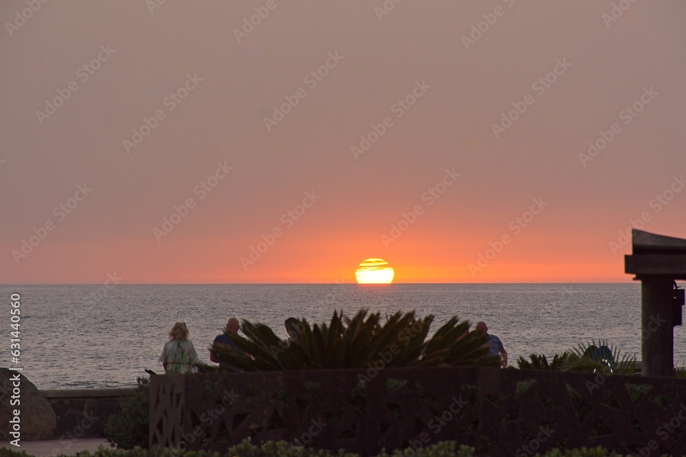 Silhouette of group of people  seeing the sun setting down in the horizon, in Maspalomas, Gran Canaria, Spain