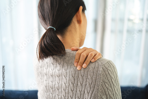 Young woman has problem with structural posture back neck and shoulder pain. Massaged her neck and shoulders for relief. reduce muscle tension on sofa couch in living room photo