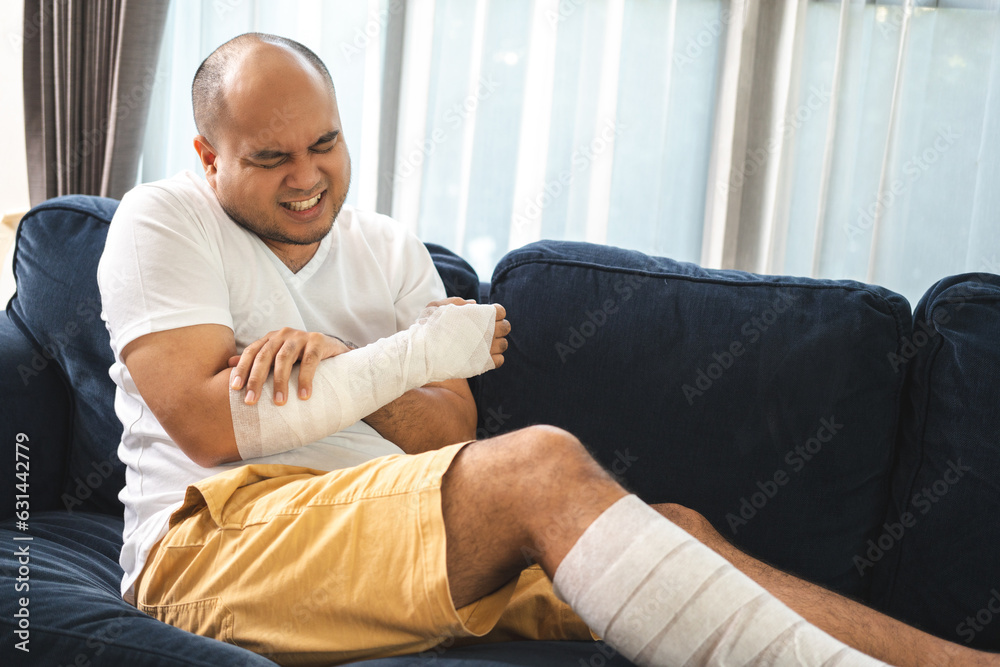 Social security and health insurance concept. Young Man suffer pain from accident fracture broken bone injury with arms splints in cast sling support arm in living room.