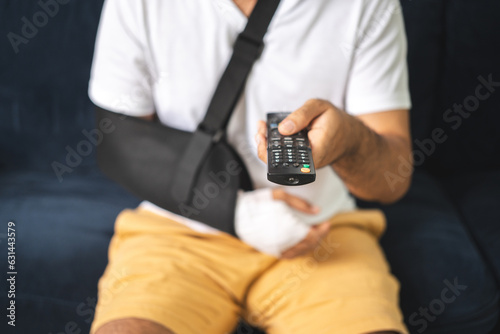 Social security and health insurance concept. Young Man suffer pain from accident fracture broken bone injury with arms splints in cast sling support arm watching tv in living room.