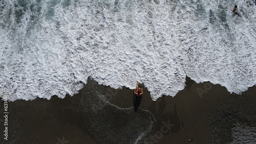 Fotografia aerea di giovane donna sulla spiaggia con costume sportivo da nuoto bagnata dalle onde dell'oceano - Vacanza al mare  photo