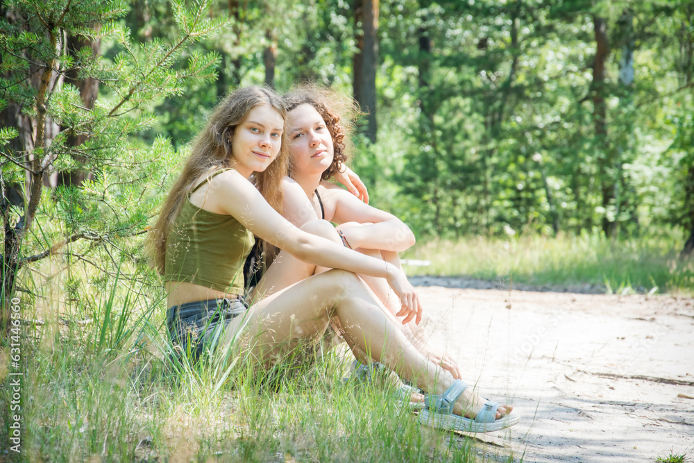 In summer, two girls girlfriends sit on the grass in the forest. In summer, two girls girlfriends sit on the grass in the forest.