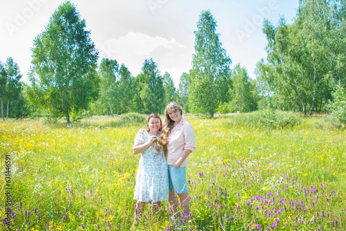 In summer, two women girlfriends are standing on a flower meadow. They are happy.