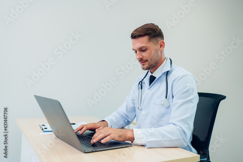 Male Doctor expert wearing white coat using laptop and reading clipboard report at work in hospital.