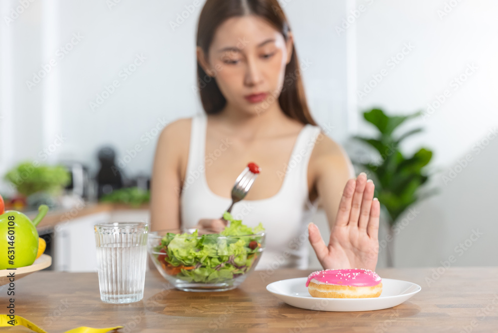 Woman on dieting for good health concept. Close up female using hand push out her favourite donut and choose salad vegetables for good health.