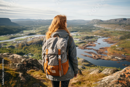 Female hiker wearing casual clothes admiring a scenic view from a mountain top. Adventurous young girl with a backpack. Hiking and trekking on a nature trail. Traveling by foot.