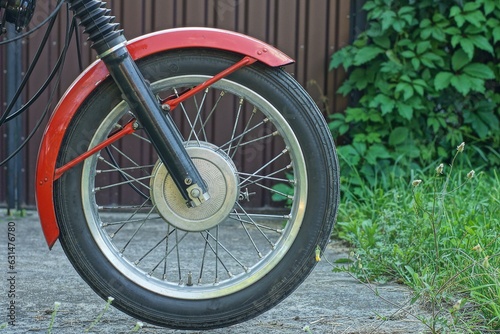 one front old retro wheel with fork part and red color front iron fender of old classic java motorcycle outdoors on the street near brown fence 