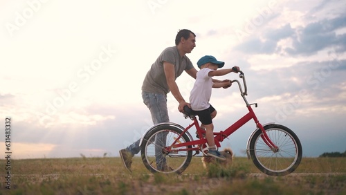 dad teaches son to ride a bike. happy family kid dream concept. the boy sat on bicycle for the first time, his father teaches boy to ride a bicycle. dog runs with family, lifestyle fun family pastime