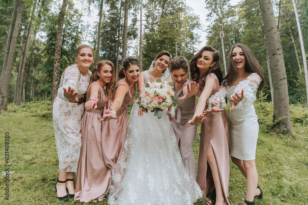 A group of beautiful girls with a bride in identical dresses are smiling, celebrating and having fun together against the background of nature and tall trees. Girls party