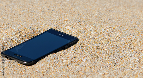cell phone buried in the sand of a majestic beach on a summer day in high resolution and sharpness, technology concept