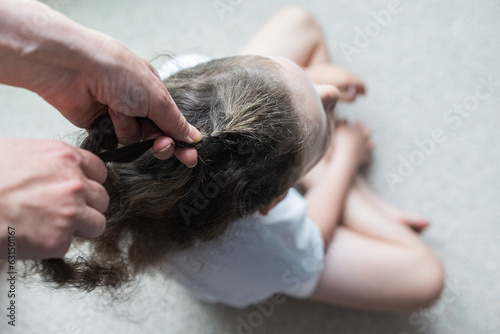 Caucasian boy sitting on the floor while his mom brushing and fixing his hair
