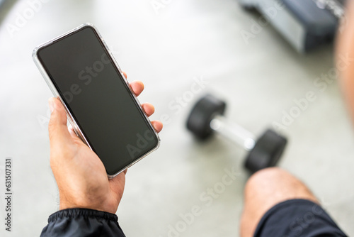 Young Athlete fitness Man Using smartphone in gym. Male Holding Cell Phone Fitness App