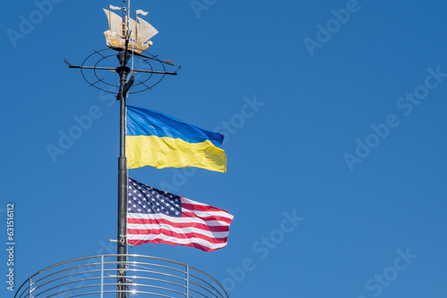 The flags of Ukraine and the USA flutter on a flagpole against a blue sky. State symbol. Ukrainian blue and yellow flag. Wind day outdoor.