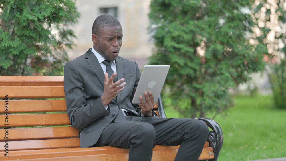 African Businessman Upset by Loss on Tablet while Sitting Outdoor on a Bench African Businessman Upset by Loss on Tablet while Sitting Outdoor on a Bench