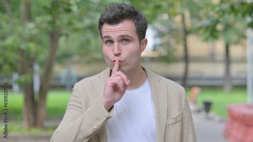 Outdoor Portrait of Casual Young Man with Finger on Lips Outdoor Portrait of Casual Young Man with Finger on Lips