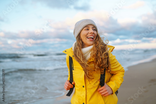 Foto Young woman tourist in a yellow coat walks along the seashore, enjoys the seascape at sunset