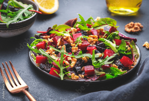 Photography Vegan salad with beet, dried plums, arugula, swiss chard and walnuts, black stone table background