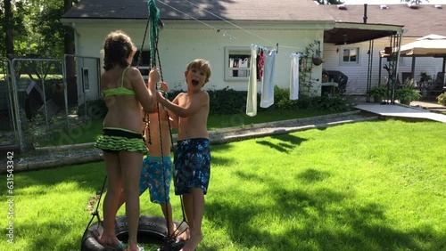 Kids happily swing on a car tire in the backyard of their house