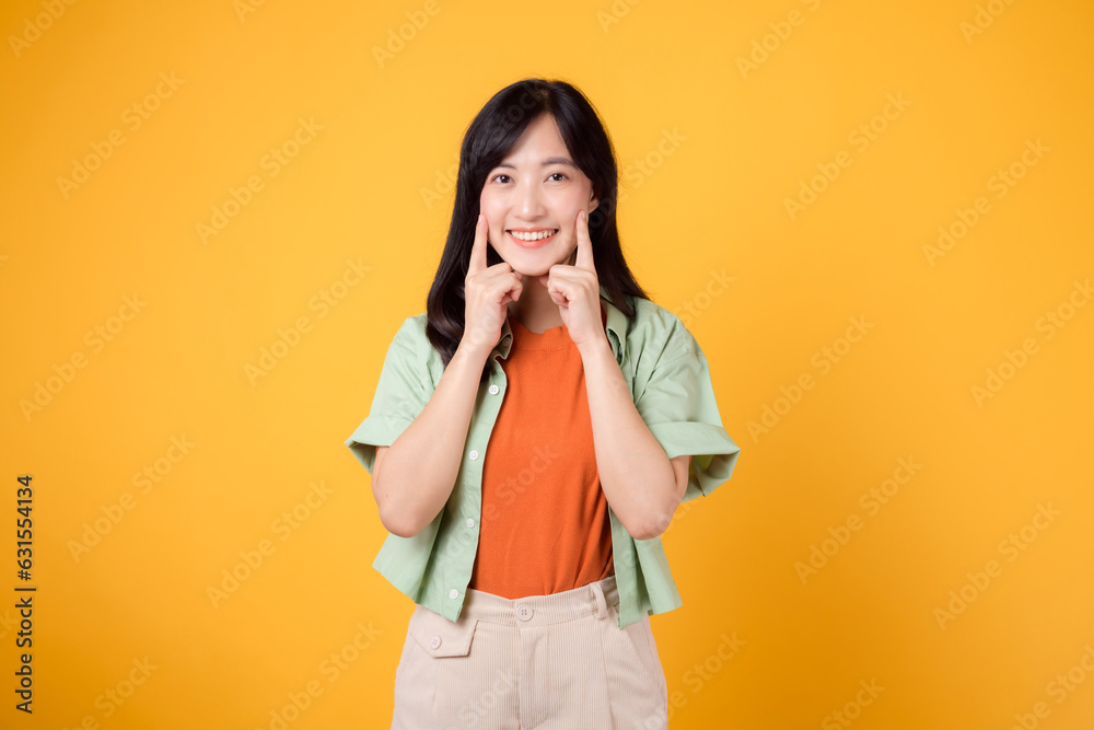 dental care with young Asian woman 30s, dressed in orange shirt and green jumper points to her teeth, isolated on a vibrant yellow background, highlighting the importance of dental healthcare dental care with young Asian woman 30s, dressed in orange shirt and green jumper points to her teeth, isolated on a vibrant yellow background, highlighting the importance of dental healthcare