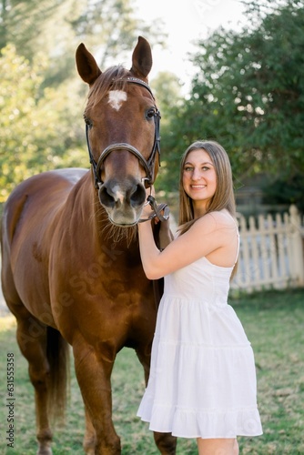 Young girl wearing a white dress petting her brown horse
