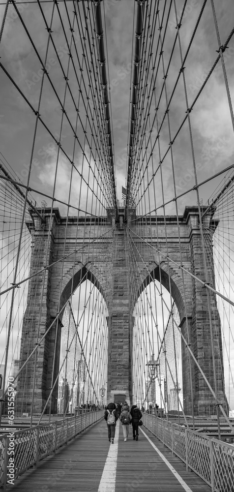 Fototapeta premium Vertical grayscale shot of people walking on Brooklyn Bridge in NYC, USA