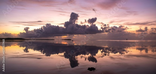Tranquil pink sunset with large fluffy clouds over the sea reflecting on the water