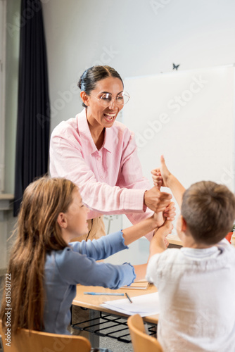 Vertical foto of happy children play clapping hands with teacher in classroom. Joyful kids with young Middle Eastern teacher playing together at break. The concept of creative learning with play