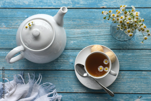 Quadro su tela Cup of chamomile tea with teapot and camomile flowers on blue wood background