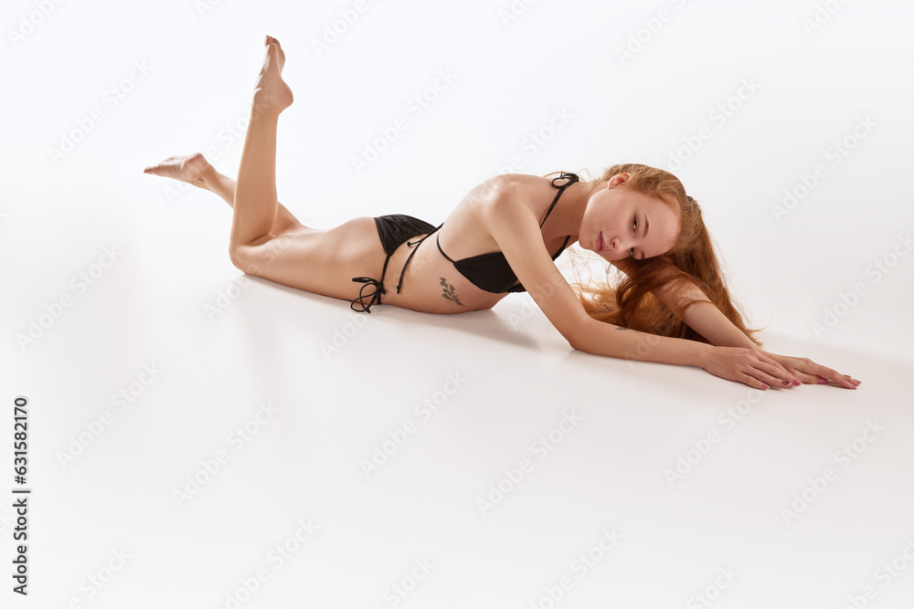 Sensual young beautiful girl lying on floor and posing in black underwear against white studio background.