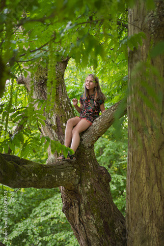 Kid climbing a tree, sitting on a branch. Luxembourg city park. Child smiling on a sunny day in the summer. 8 year old girl. photo