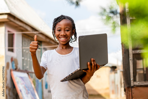 A young girl holding a laptop and giving a thumbs up photo