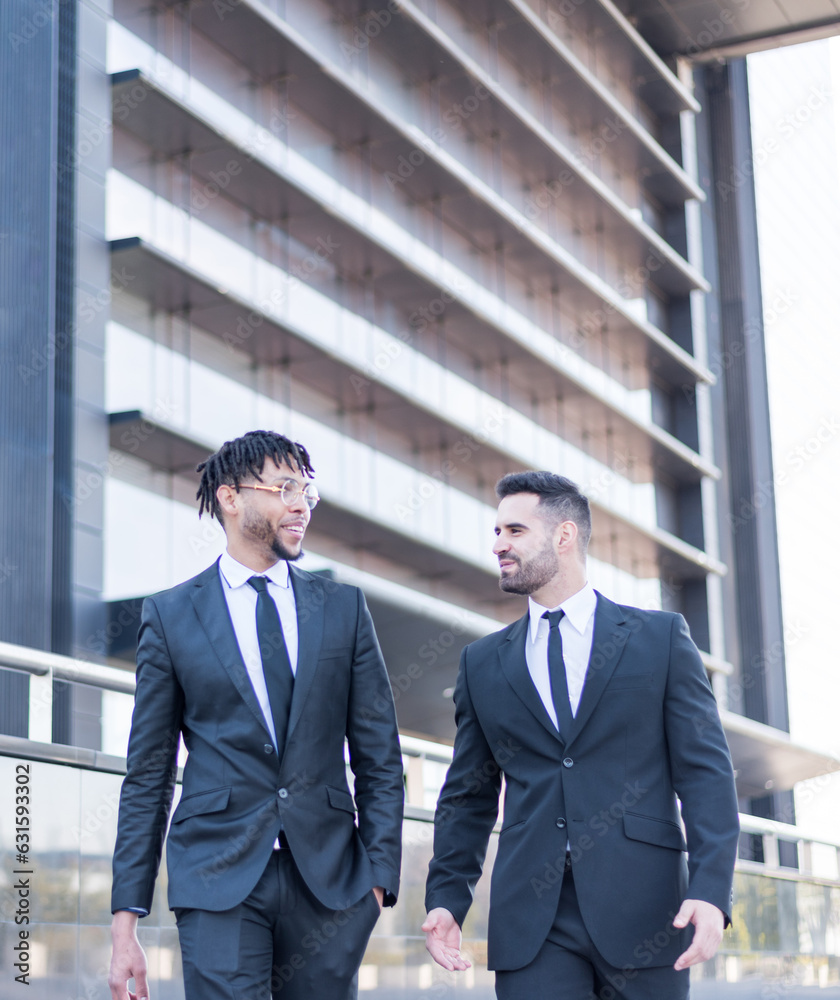 businessmen wearing suits walking and smiling and talking outdoor in a business area. businessmen wearing suits walking and smiling and talking outdoor in a business area.