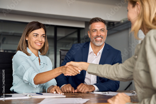 Fotografija Mature Latin business team of woman and European business man shaking hands with colleagues, partners or employees, signing a contract