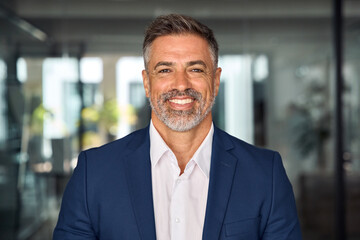 Headshot close up portrait of indian or latin confident mature good looking middle age leader, ceo male businessman in suit on office background. Handsome hispanic senior business man smile at camera.