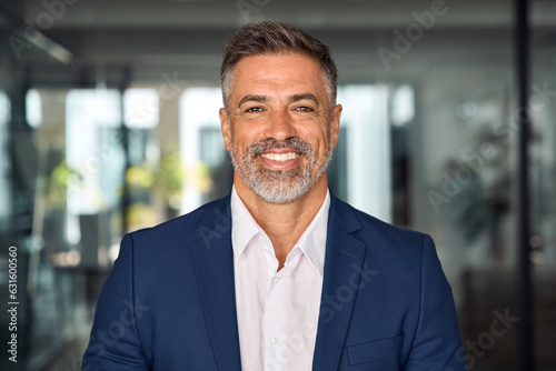 Headshot close up portrait of indian or latin confident mature good looking middle age leader, ceo male businessman in suit on office background. Handsome hispanic senior business man smile at camera.