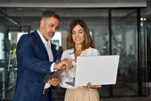 Mature Latin business man and European business woman discussing project on laptop gadget in office. Two diverse partners, colleagues, team of confident professional business people work together. © Stock 4 You
