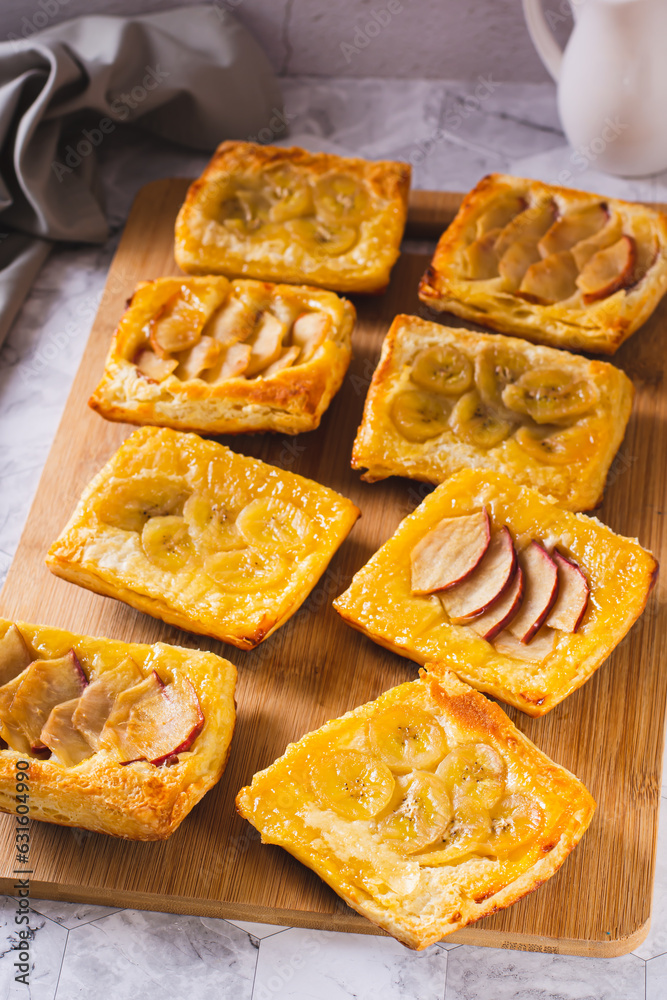 Small upside-down puff pastry cakes with banana and apple on a board vertical view