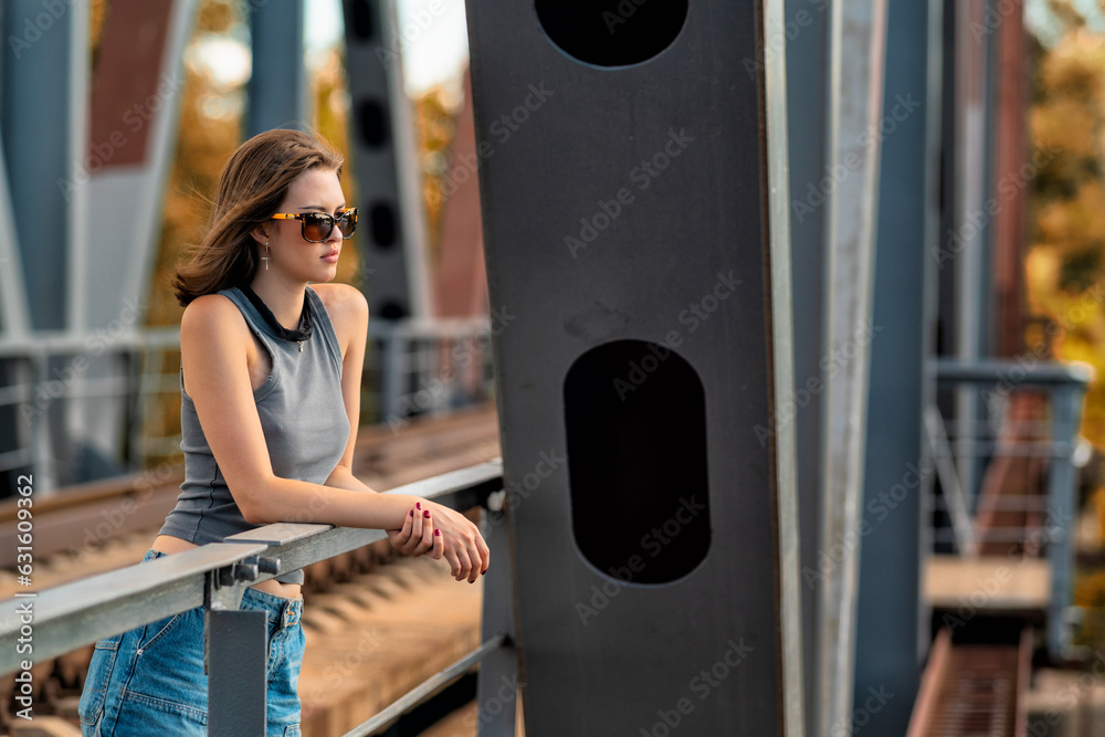 The girl is standing on the bridge leaning on the railing