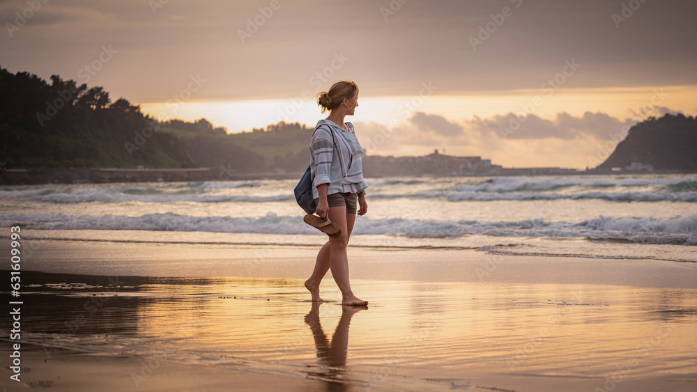 Woman walking barefoot on beach in beautiful sunset 