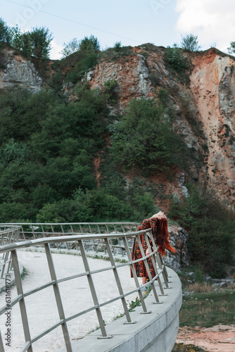 Red-haired confident full-length girl in an ethnic dress on a career background. Huge stones. Red hair develops in the wind. Concept. A symbol of will and indomitability photo