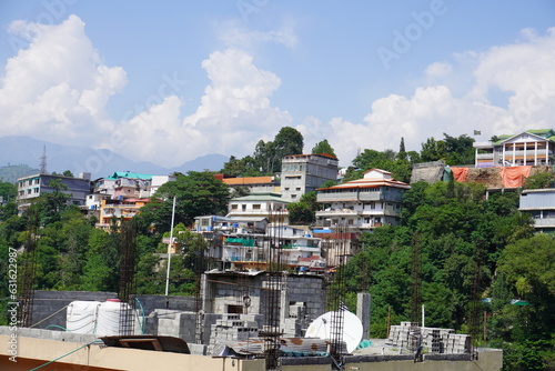 A vibrant view of Muzaffarabad, featuring colorful houses nestled among green trees with a backdrop of mountains and a clear blue sky photo