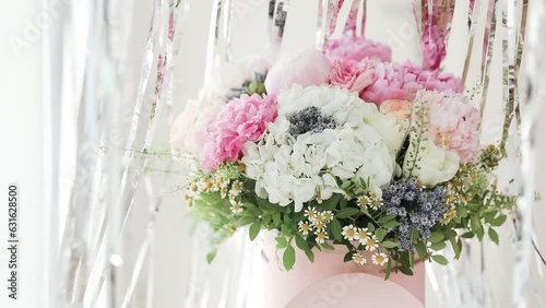 An elegant bouquet of fresh roses, peonies, and daisies in a pink box, beautifully arranged and placed by a light-filled window.
