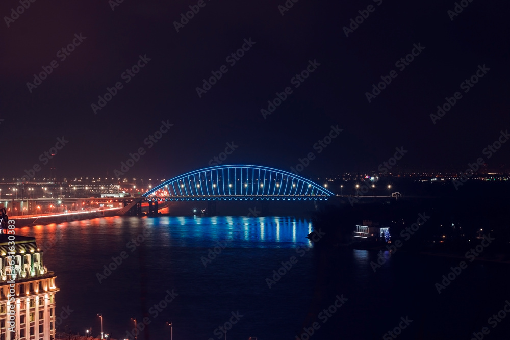 Night city minimal landscape. Dark and tranquil long exposure photography with led illuminated bridge and light reflections in the water. Bridge across the Dnipro river, Kyiv, Ukraine