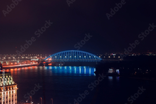 Night city minimal landscape. Dark and tranquil long exposure photography with led illuminated bridge and light reflections in the water. Bridge across the Dnipro river, Kyiv, Ukraine © Тамара Печеная