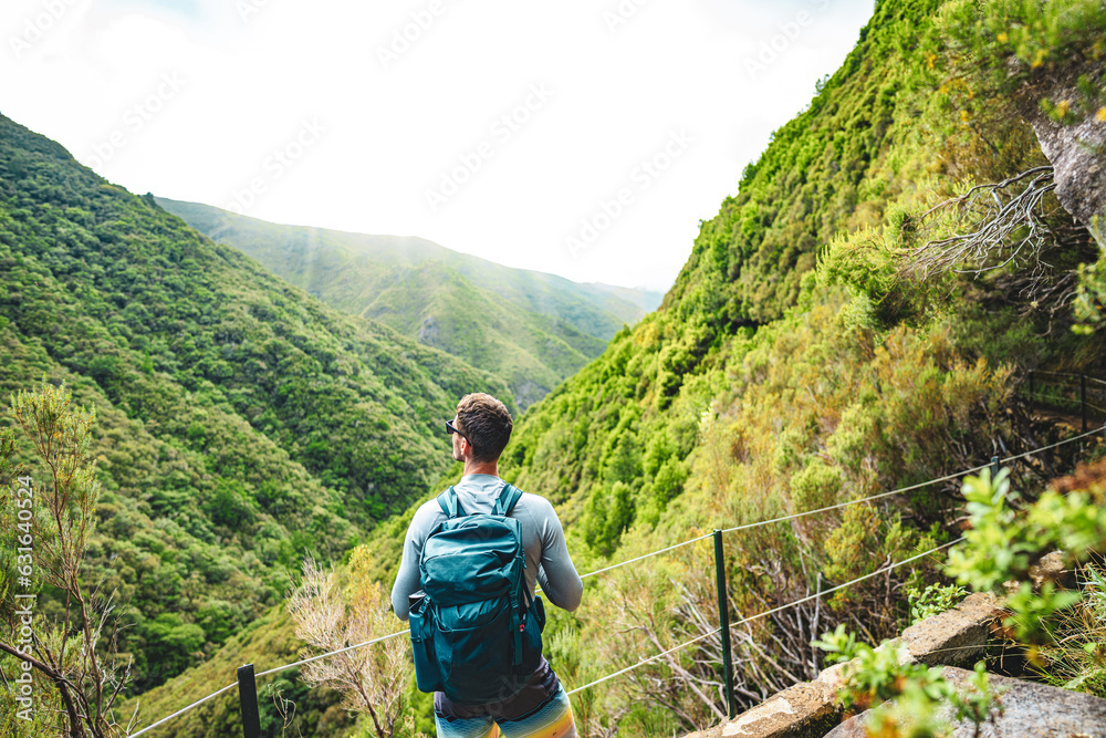 Backpacker watching the hills of the Madeiran forest from the water channel path on a sunny day. 25 Fontes Waterfalls, Madeira Island, Portugal, Europe.