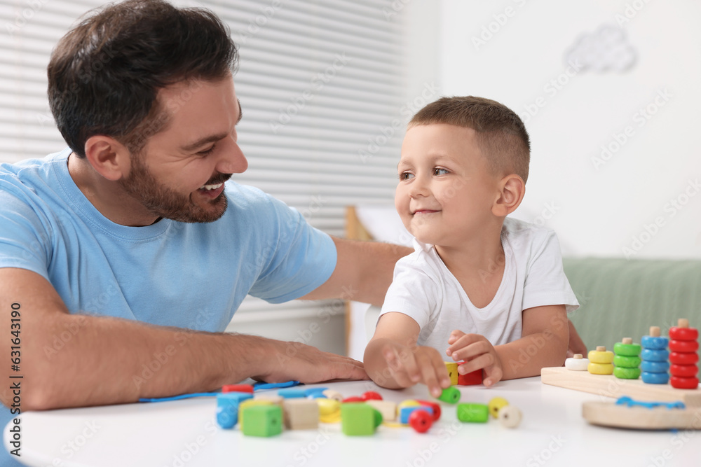 Motor skills development. Father and his son playing with colorful wooden pieces at table indoors Motor skills development. Father and his son playing with colorful wooden pieces at table indoors