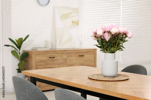 Vase with pink peonies on wooden table in dining room