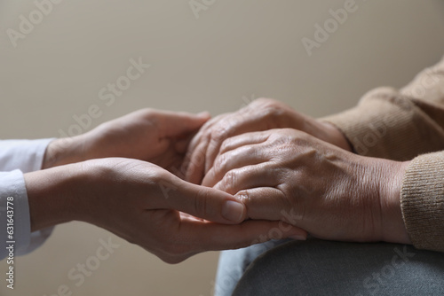 Woman holding hands with her mother on beige background, closeup