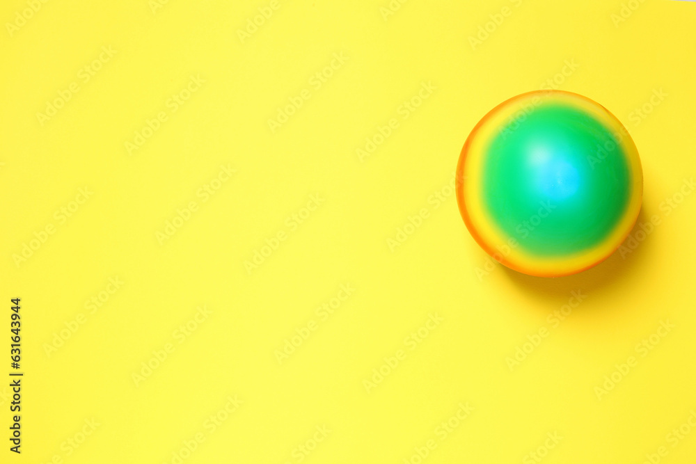 New bright kids' ball on yellow background, top view. Space for text